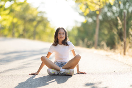 Young girl sitting on sunlit road outdoorsの写真素材
