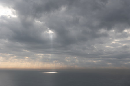 The sun rays breaking through gray clouds reflecting on the sea surfaceの写真素材