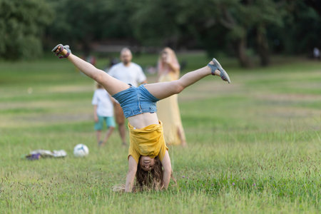 Young girl doing a cartwheel in the park while family watchesの写真素材