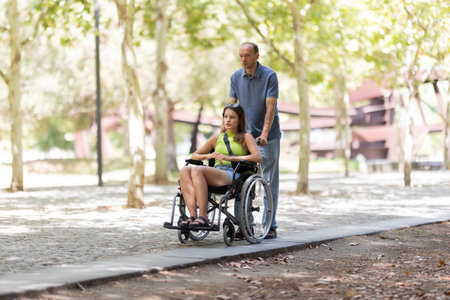 Father pushing daughter in wheelchair in park during sunny dayの写真素材