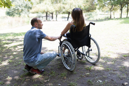 Man assisting woman in wheelchair in park