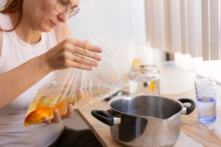 Woman holding plastic bag with goldfish over pot in kitchenの写真素材