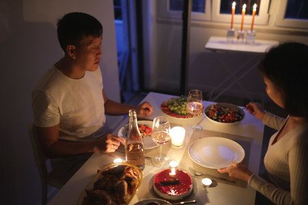 Couple enjoying romantic candlelit dinner at home with wine and cakeの写真素材