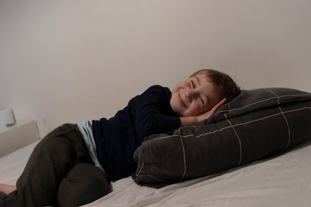 Smiling child relaxing on bed with pillow: sweet dreams and happy childhoodの写真素材