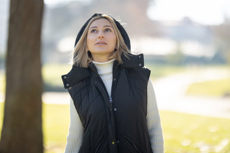 Woman wearing vest and looking up in a park during a sunny day