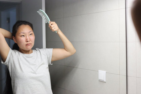 Young woman combing hair in bathroom mirrorの写真素材