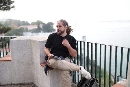 Thoughtful male writer taking notes sitting on viewpoint in lisbon