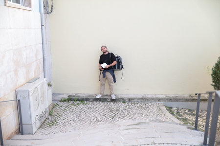 Tourist reading travel guide while leaning against wall in lisbon