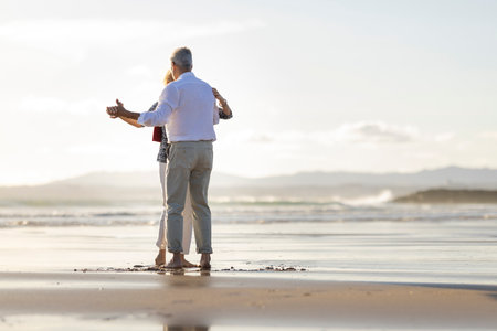 Senior couple dancing barefoot on the beach at sunsetの写真素材