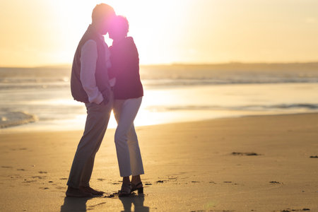 Senior couple embracing on beach at sunset: romantic golden hour strollの写真素材