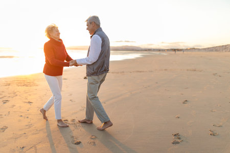 Happy senior couple dancing barefoot on the beach at sunsetの写真素材