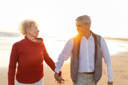 Happy senior couple holding hands and walking on the beach at sunsetの写真素材