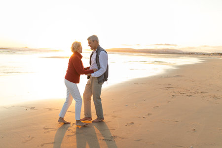 Happy senior couple dancing barefoot on the beach at sunsetの写真素材