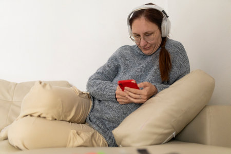 Woman relaxing on sofa using smartphone and wearing headphonesの写真素材
