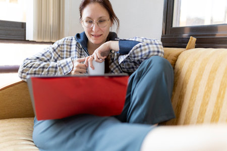 Woman working from home using laptop and drinking teaの写真素材
