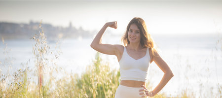 Young fitness model showing biceps muscle in nature backgroundの写真素材