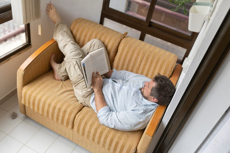 Man relaxing on sofa reading a book in living roomの写真素材