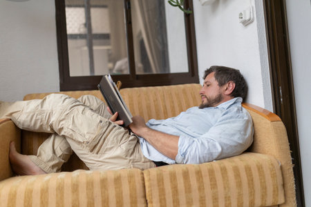 Man relaxing on sofa reading a book at homeの写真素材