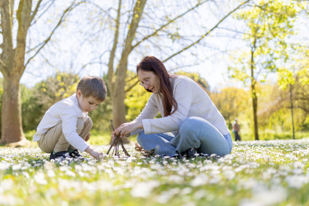 Mother and son building a small teepee with twigs in a field of daisiesの写真素材