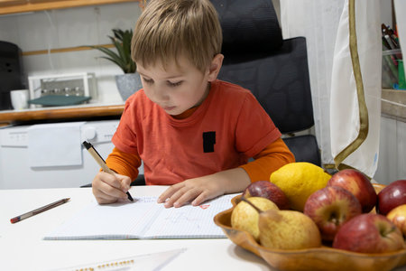 Young boy doing homework and drawing in notebook at homeの写真素材