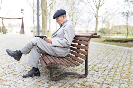 Senior professor writing notes while sitting on bench in parkの写真素材
