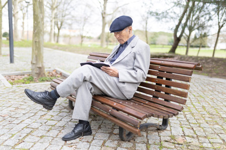 Elderly asian man sitting on bench writing in notebook in parkの写真素材