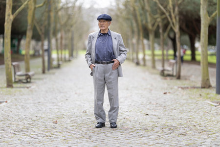 Senior man wearing grey suit and flat cap standing in parkの写真素材