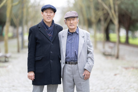 Adult son posing with elderly father in park wearing newsboy capsの写真素材