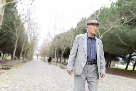 Elderly asian man walking in a cobblestone park wearing a gray suit and listening to musicの写真素材