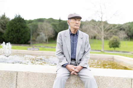 Elderly man sitting pensively by a fountain in a parkの写真素材