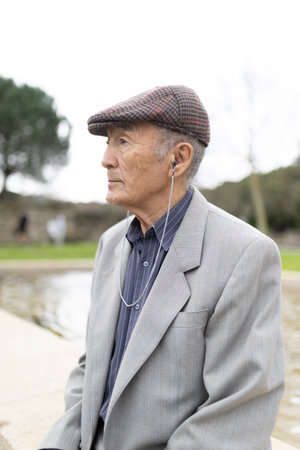 Elderly gentleman wearing earphones and listening to music in parkの写真素材