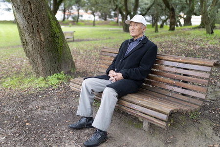 Senior man relaxing on park bench listening music with earphonesの写真素材