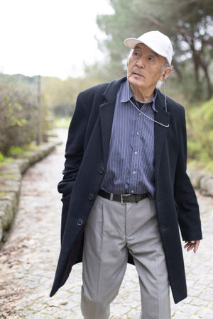 Elderly asian man walking in park wearing a cap and coatの写真素材