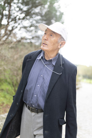 Elderly asian man listening music while walking in parkの写真素材