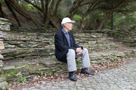 Senior man listening music sitting on stone steps in parkの写真素材