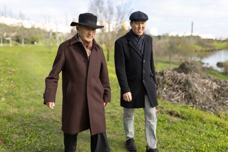 Elderly man and son walking together in park by lakeの写真素材