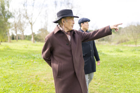 Elderly man pointing while walking in park with younger manの写真素材