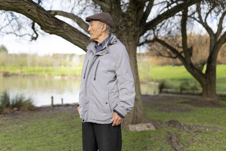 Senior man enjoying relaxing walk in peaceful park by lakeの写真素材