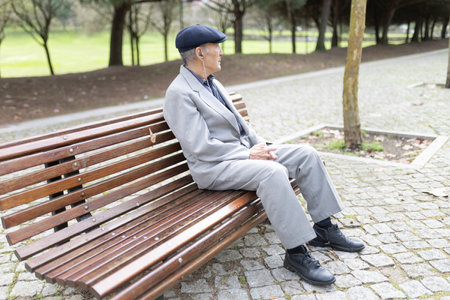 Elderly gentleman sitting on bench listening music in parkの写真素材