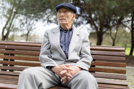 Elderly man listening music sitting on bench in park