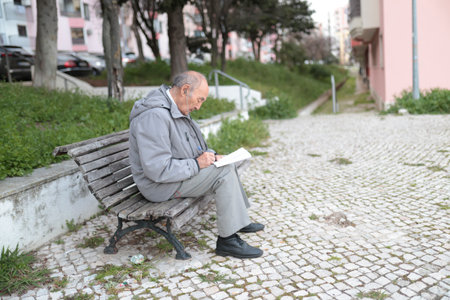 Senior man writing on paper while sitting on bench outdoorsの写真素材