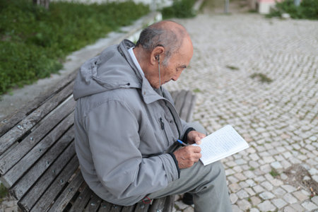 Elderly man writing on notebook while sitting on benchの写真素材