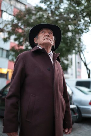 Senior man wearing hat and coat looking up in the cityの写真素材
