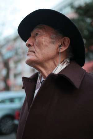 Elegant senior man wearing hat and listening music in city streetの写真素材