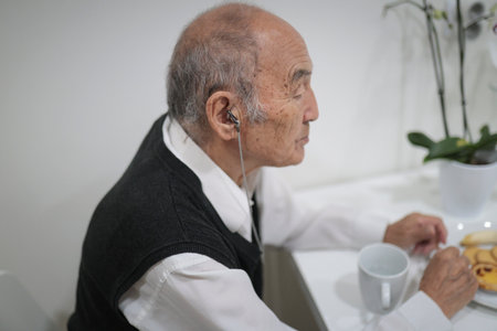 Elderly man wearing hearing aid enjoying breakfast at homeの写真素材