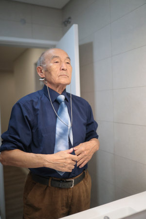 Senior businessman adjusting clothes in bathroom mirror with hearing aid