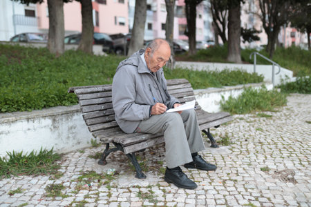 Senior man writing on paper while sitting on bench in parkの写真素材