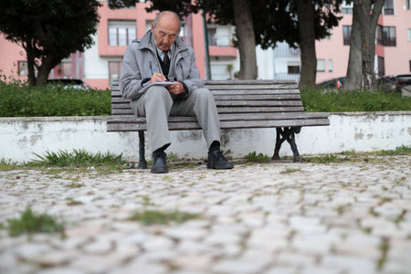Senior professor writing notes while sitting on bench in parkの写真素材