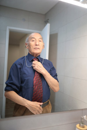 Elegant senior man adjusting his tie in bathroom mirrorの写真素材