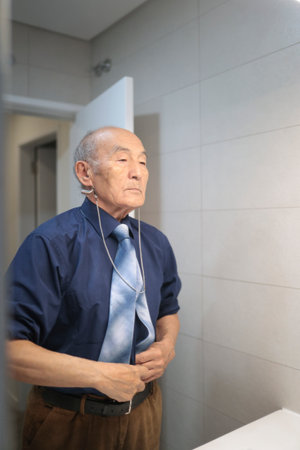 Senior businessman getting ready in bathroom, adjusting his tie and beltの写真素材